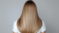 Young woman with long straight blonde hair from behind wearing white t-shirt against gray background, showing healthy shiny hairstyle after salon treatment.