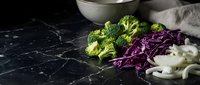 Fresh broccoli, purple cabbage and white mushrooms arranged on dark marble surface for healthy cooking and meal preparation.