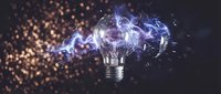 Exploding light bulb with purple electric energy and glass fragments against dark background with golden bokeh lights for creative innovation concepts.