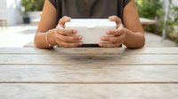Close-up of female hands holding blank white tablet device on wooden table outdoors, suitable for app promotion and digital marketing campaigns.