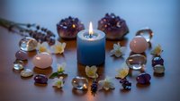 Blue candle flame surrounded by rose quartz crystals, amber gems, dried flowers and pinecones creating peaceful spa meditation atmosphere.