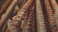 Rusty steel reinforcement bars in diagonal composition showing weathered metal texture and corrosion patterns. Construction material background with shallow depth of field.