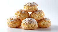 Fresh cream puffs dusted with powdered sugar arranged in pyramid shape on white background, golden pastry filled with vanilla custard cream.