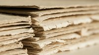 Stack of aged vintage paper sheets with worn torn edges creating textured layers for antique document backgrounds and historical design projects.