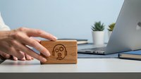 Wooden rubber stamp with sad face emoji being pressed by hand on white desk near laptop for office feedback and customer service rating.