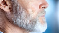 Side profile of mature man with well-groomed white beard against blue background, showing facial features in detail. Close-up portrait emphasizes natural aging and wisdom.