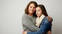 Middle-aged Caucasian mother embracing teenage daughter in warm family moment. Loving parent-child relationship showing support and connection.