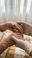 Caring hands of young caregiver gently holding elderly person's wrinkled hands in warm sunlight, showing compassion and support in healthcare setting.