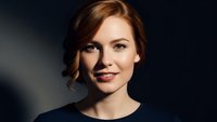 Professional young Caucasian businesswoman with auburn hair smiling confidently in corporate attire against dark background for business presentations.