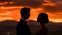 Romantic couple silhouettes against dramatic orange sunset sky with mountains, wedding photography concept for love and relationship themes.