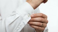 Man buttoning white dress shirt cuff, wearing a ring, close-up detail shot for fashion, wedding, and business style concepts.