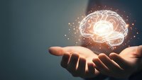 Human hand holding glowing brain hologram with sparkling particles representing artificial intelligence, neuroscience and mental health concepts.