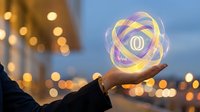 Businessman holding glowing digital atom symbol with zero in center against blurred city lights at dusk, representing innovation, technology, and nuclear energy concepts.