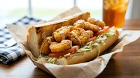 Crispy fried chicken sandwich with golden breaded pieces in fresh bun on parchment paper, served with orange drink for casual dining and fast food menu.
