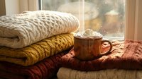 Stacked knit sweaters and warm beverage by window on autumn day, cozy fall home decor and seasonal comfort styling.