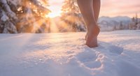 Bare feet walking through fresh snow at golden hour sunset with warm sunlight creating magical sparkles and footprints in pristine winter landscape.