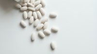 White oval pills and capsules scattered on neutral background, suitable for pharmaceutical, healthcare, medical, and wellness industry applications.