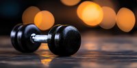 Black dumbbell on wooden surface with warm bokeh lights in background, reflecting fitness motivation and strength training concept for gym marketing.