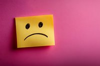 Yellow sticky note with hand drawn sad face on vibrant pink background showing negative emotion, depression or bad customer experience concept.