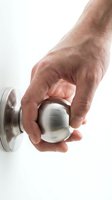 Male hand turning modern stainless steel door knob on white background isolated for home security and interior design concepts.