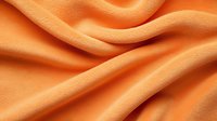 Soft orange fleece fabric with gentle folds and waves creating abstract texture pattern. Macro close up view shows detailed textile surface structure.
