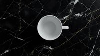 Empty white ceramic cup on black marble surface with gold veining, overhead view, minimalist flat lay composition for beverage, coffee, or kitchen design projects.