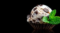 Chocolate mint ice cream scoop garnished with fresh mint leaves in dark chocolate shell cup against black background, selective focus on creamy texture.