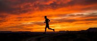 Silhouette of male runner jogging on rocky terrain against dramatic orange and red sunset sky, suitable for fitness, wellness, and sports marketing.