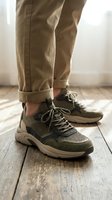 Close-up of male legs in beige chinos and olive green sneakers standing on wooden floor. Casual menswear and footwear styling for everyday comfort and fashion.