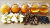 Homemade apple cider ingredients with fresh sliced apples, honey jars, cinnamon sticks, star anise, allspice berries and juniper berries on wooden background.
