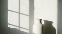 Ceramic pitcher casting shadow on white wall with window light creating geometric patterns, suitable for minimalist home decor and interior design projects.