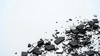 Broken black charcoal pieces and powder scattered on white background, isolated for design projects and artistic compositions.