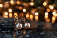 Elegant pearl drop earrings on dark surface with warm bokeh lights background creating romantic atmosphere. Perfect for jewelry advertising and fashion blogs.