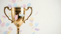 Golden trophy cup with ornate handles on pastel confetti background symbolizing victory, achievement, success, competition winner, celebration moment.