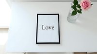 Framed Love print on white desk beside pink rose in glass vase, minimalist romantic home decor for Valentine's Day and wedding.