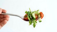 Fresh mixed salad with arugula, tomatoes and herbs on fork isolated on white background for healthy eating and diet concepts.