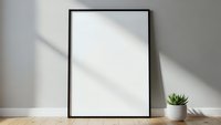 Blank white poster frame mockup on wooden shelf with small plant and natural window shadows for artwork display and interior design presentations.