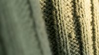 Close-up of cozy knitted wool sweater texture showing cable patterns and stitches in warm beige tones for fashion and textile design projects.