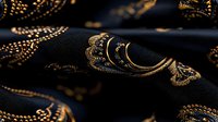 Luxurious black fabric with ornate golden oriental pattern creates elegant waves and folds. Decorative textile with metallic embroidered traditional motifs on dark background.