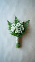 Small rustic wedding boutonniere with white flowers and green fern leaves wrapped in twine on neutral background for ceremony decoration.