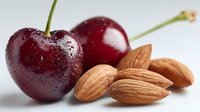 Fresh ripe cherries with water droplets paired with raw almonds on white background, showcasing healthy natural snack options.
