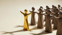 Golden figure stands out from crowd of wooden people with raised arms showing leadership confidence and individuality in business teamwork concept.