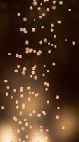 Warm golden bokeh lights scattered across dark brown background, creating soft out-of-focus circular light effects. Suitable for festive, holiday, celebration, and elegant design projects.