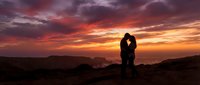 Silhouetted couple embracing at sunset with dramatic orange and red sky, romantic landscape scene for love and relationship concepts.