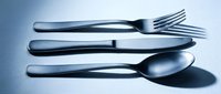Shiny stainless steel fork, knife, and spoon arranged on a light surface with cool blue tones, casting soft shadows for restaurant menus.