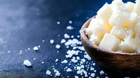 Coarse white sea salt crystals in wooden bowl on dark blue surface with scattered grains and copy space for culinary and cooking designs.