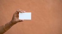 Cropped hand of Black man holding blank white business card against warm beige background, ready for branding and corporate design projects.