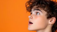 Young male model with curly brown hair expressing surprise against vibrant orange background, profile view showing defined facial features and open mouth.