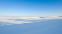Frozen lake landscape with snow-covered surface under clear blue sky, suitable for winter backgrounds, nature scenes, and seasonal design projects.