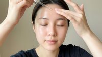 Young Asian woman applying facial serum with dropper on forehead, eyes closed, skincare routine concept for beauty and wellness content.